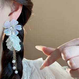 Close-up of elegant iridescent acrylic flower earrings with pearl tassels on a model's ear