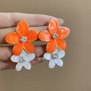Dettaglio di orecchini a fiore in smalto arancione e bianco con strass brillanti.