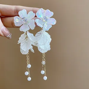 Macro view of elegant iridescent acrylic flower earrings with gold chains and pearls.