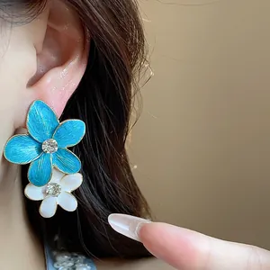 Dettaglio di orecchini a fiore in smalto blu e bianco con strass centrale brillante