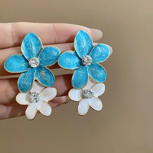 Dettaglio ravvicinato di orecchini a fiore in smalto blu e bianco con strass brillanti