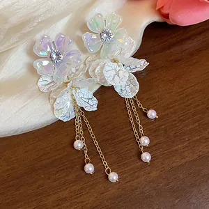 Detailed close-up showing iridescent acrylic flower earrings with gold chains and white pearls