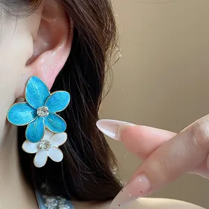 Primo piano di orecchini a fiore in smalto blu e bianco con strass sull'orecchio.