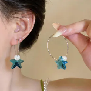 Primer plano detallado de pendientes de aro con estrella de cristal azul y perla en la oreja