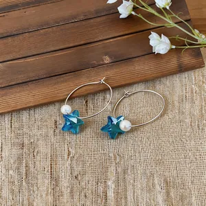 Detalle de aros con estrellas azules y perlas blancas para un estilo de vacaciones.