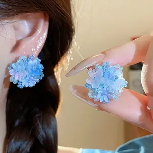 Gros plan sur d'exquises boucles d'oreilles fleurs en perles bleu clair aux pétales translucides