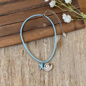 Detalle de collar de cuentas azul claro con dijes de concha plateada y estrella de mar azul