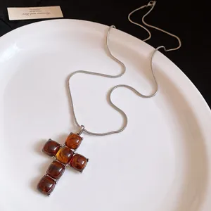 Detailed close-up of a vintage resin cross pendant on a sleek silver snake chain necklace