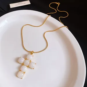 Detailed close-up of minimalist white resin cross pendant with golden snake chain.