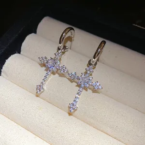 Detailed close-up view of silver zircon cross pendant earrings on a beige jewelry display