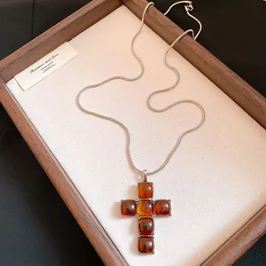 Detail showing a minimalist resin cross pendant with amber beads on a silver snake chain
