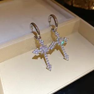 Close-up of silver-tone cross pendant earrings with shimmering cubic zirconia stones.