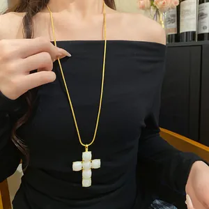 Detailed macro view of white resin cross pendant on a sleek gold-colored snake chain necklace.