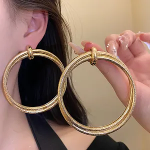 Detailed view of oversized double hoop gold earrings featuring a pleated metal texture