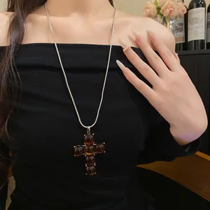 Amber-colored resin cross pendant necklace on a silver snake chain worn by a fashion model