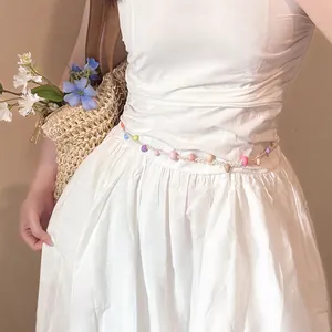 Dettaglio di una catena in vita bohémien con perle in resina colorata su un abito bianco