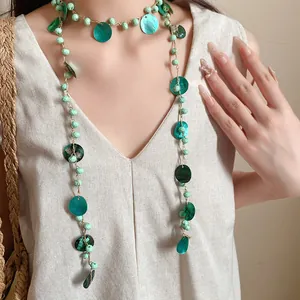 Dettaglio di una collana bohémien con perline verdi e ciondoli in conchiglia naturale su modella