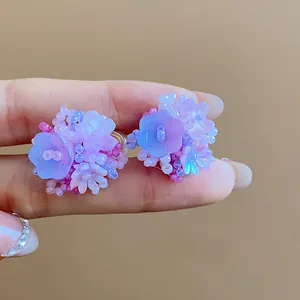 Gros plan de délicates boucles d'oreilles fleurs en perles de verre violettes et bleues.