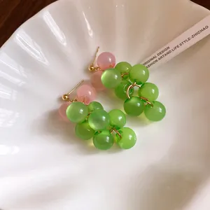 Close-up detail of sweet green and pink resin grape bead earrings placed in a shell tray.