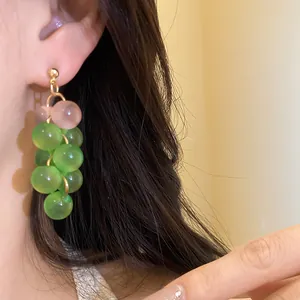 Detail view showing green and pink resin beaded grape-style drop earrings worn on an ear model