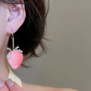 Nahaufnahme eines rosa Harz-Erdbeer-Ohrrings mit Strasssteinen am Ohr eines Models