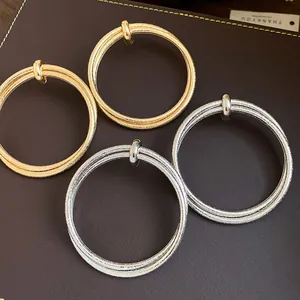 Macro view of textured gold and silver metal hoop earrings with a wrinkled design on leather