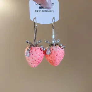Makro-Detail von süßen rosa Erdbeer-Ohrhängern aus Harz mit glänzendem CZ-Kristall.