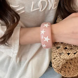 Gros plan d'un bracelet jonc en résine rose avec motif d'étoiles blanches au poignet