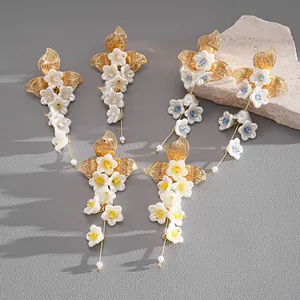 Dettaglio di orecchini floreali con nappe, fiori di vetro perlato bianco e accenti dorati.