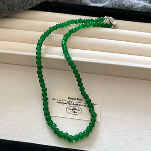 Close-up of a vintage green bead necklace displayed on a textured white jewelry tray.