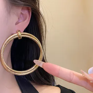 Close-up view of vintage large golden hoop earrings with a textured metal finish on a model
