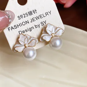 Macro detail of French-style flower pearl earrings featuring white enamel petals and gold edges