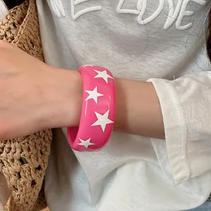 Détail d'un bracelet jonc en résine rose vif avec des motifs d'étoiles blanches