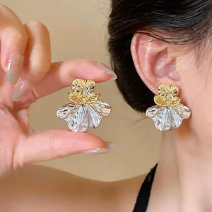 Close-up detail of elegant two-tone flower stud earrings with crystal on model's ear