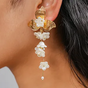 Primo piano di eleganti orecchini a fiore con nappe dorate indossati su modella