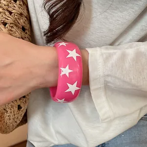 Détail d'un bracelet jonc rose épais en résine avec un motif d'étoiles blanches audacieux