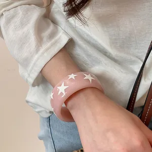 Détail d'un jonc élégant en résine rose orné d'étoiles blanches porté au poignet