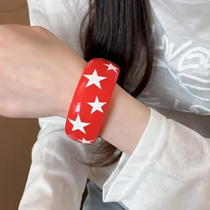 Vue détaillée d'un large bracelet en résine rouge avec des étoiles blanches au poignet