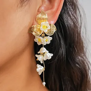 Dettaglio di orecchini a fiore dorati con petali in finta perla bianca e nappine