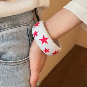 Gros plan d'un bracelet jonc en résine blanche avec des motifs d'étoiles roses éclatants