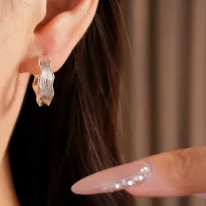 Close-up of elegant silver-colored textured wavy hoop earrings worn on a model's ear