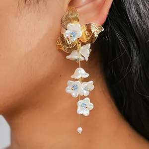 Primo piano di eleganti orecchini a nappa con fiori dorati e petali di vetro bianco