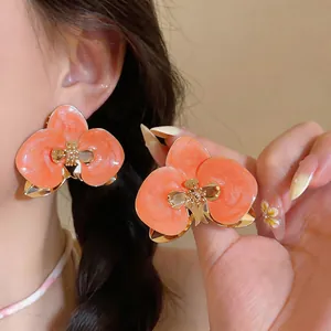 Detailansicht der eleganten orangefarbenen Emaille-Orchideen-Ohrstecker mit Goldakzenten
