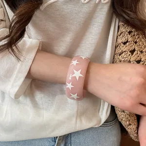 Détail d'un bracelet jonc en résine rose à motifs étoiles porté au poignet