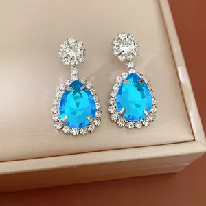 Elegant teardrop-shaped blue crystal earrings with clear rhinestone halo on jewelry box