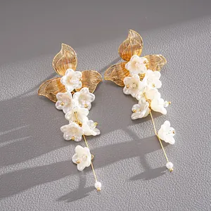 Dettaglio di orecchini a nappa con fiori bianchi, foglie dorate e perle eleganti.