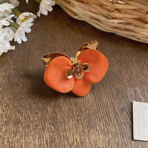 Eine detaillierte Makroansicht eines orangefarbenen Emaille-Blumenohrings auf Holz.