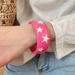 Détail d'un bracelet jonc en résine rose orné de motifs d'étoiles blanches sur un poignet