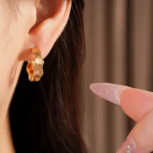 Close-up of a pleated gold hoop earring on a model's ear showing detailed texture