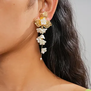 Dettaglio di eleganti orecchini a fiore dorato con nappe floreali di perle bianche